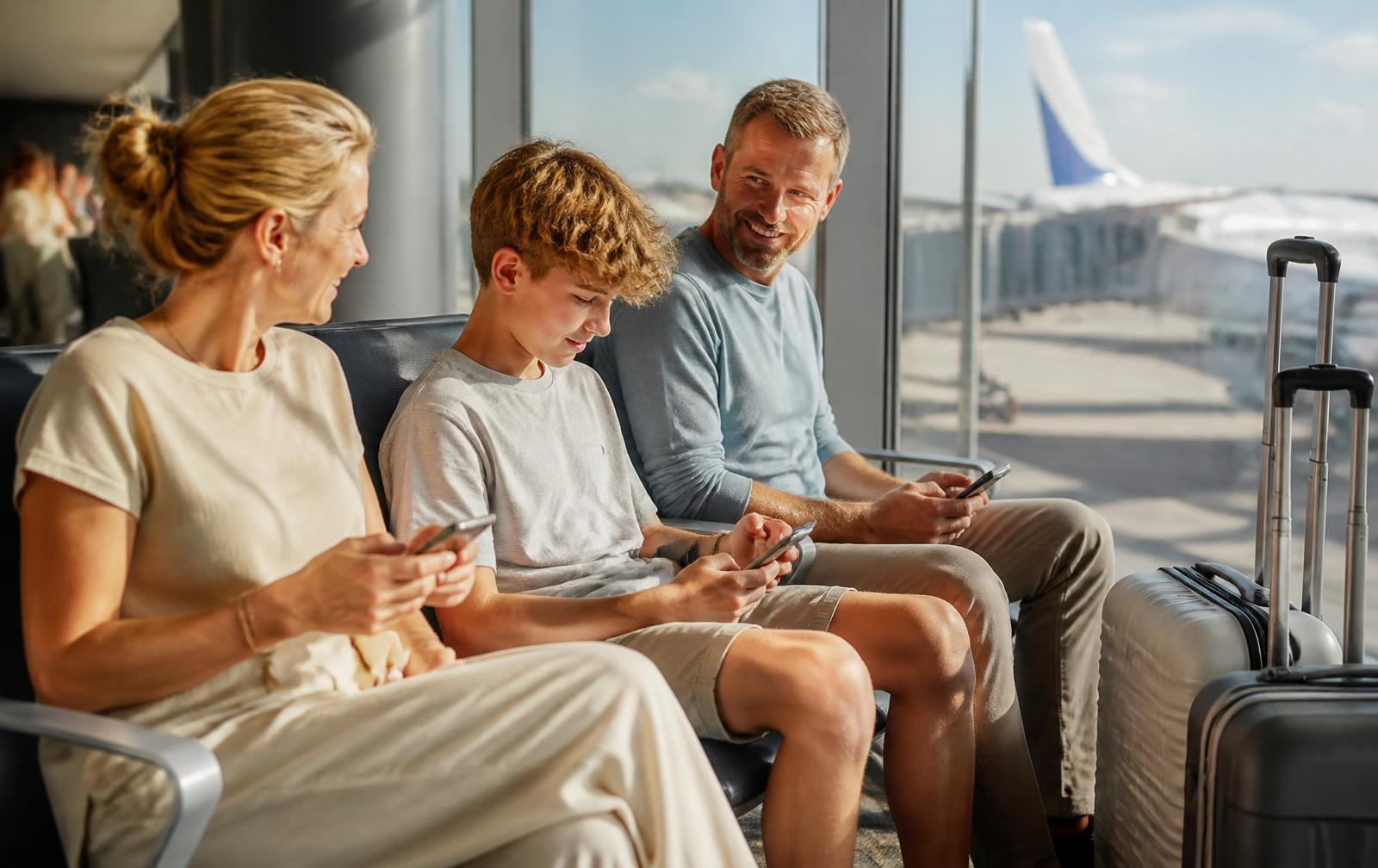 A family of three checking their phones together in an airport departure lounge